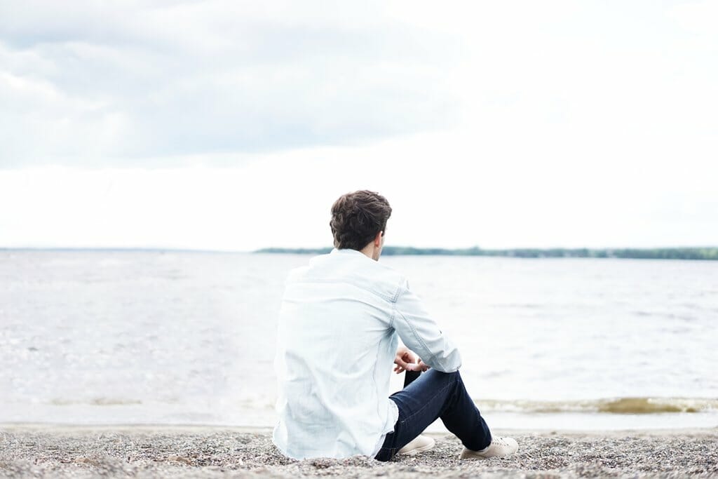 A man sitting at the beach looking at the ocean.