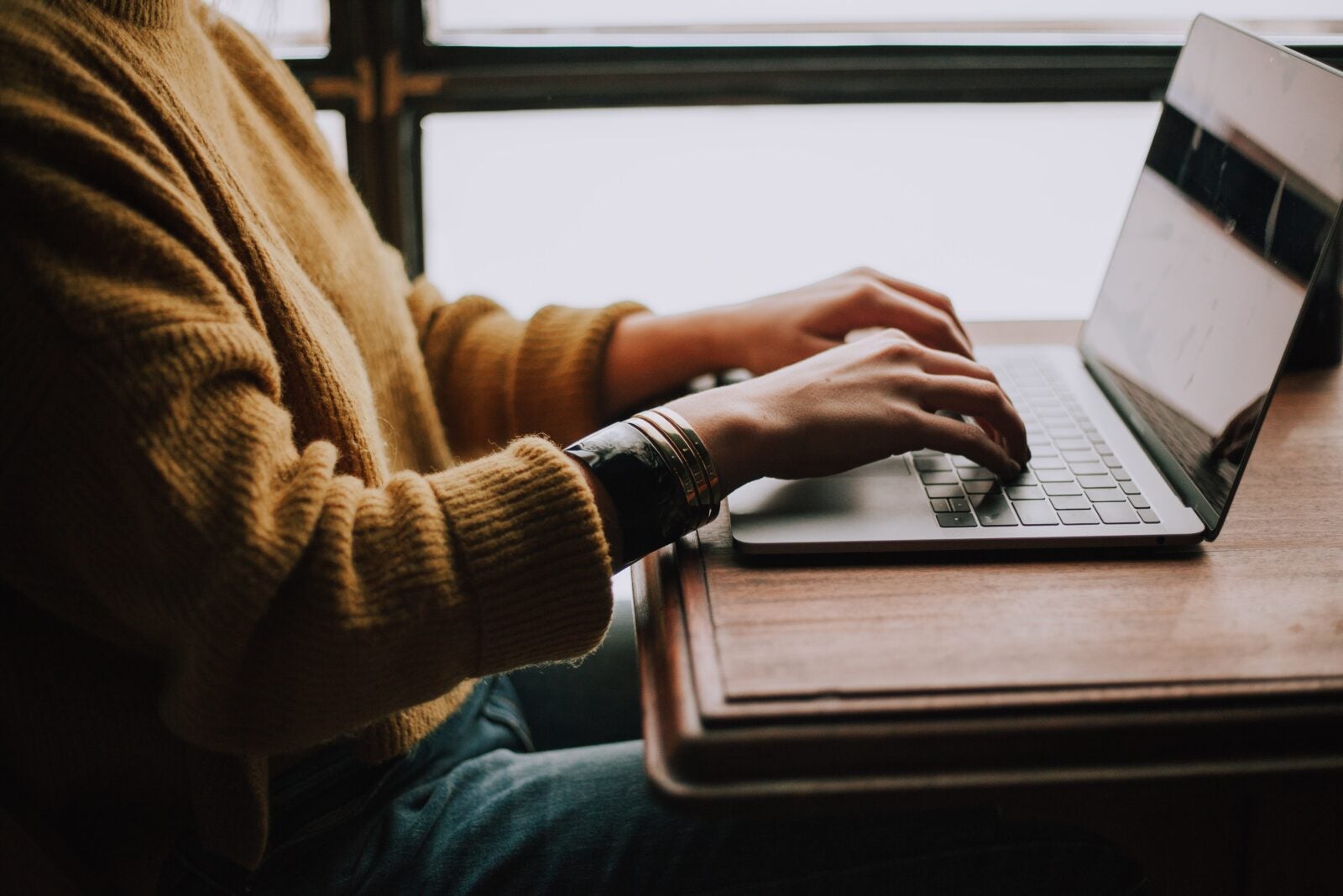 A person wearing a sweater using their laptop on a desk.