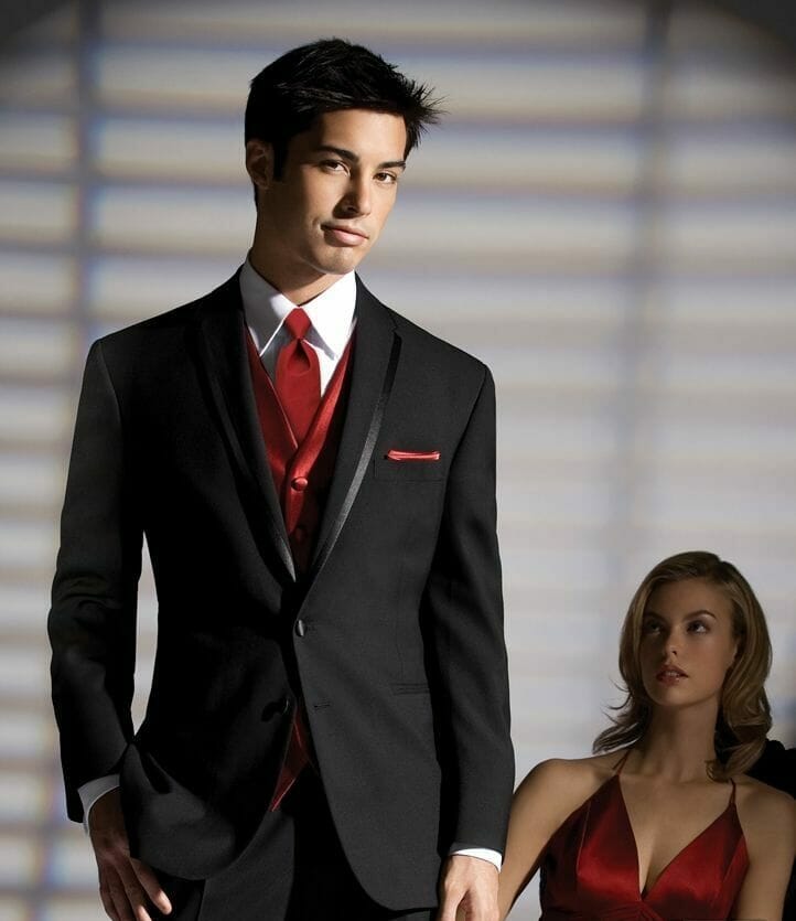 Man In A Tuxedo Posing While Woman In A Red Dress Looks On