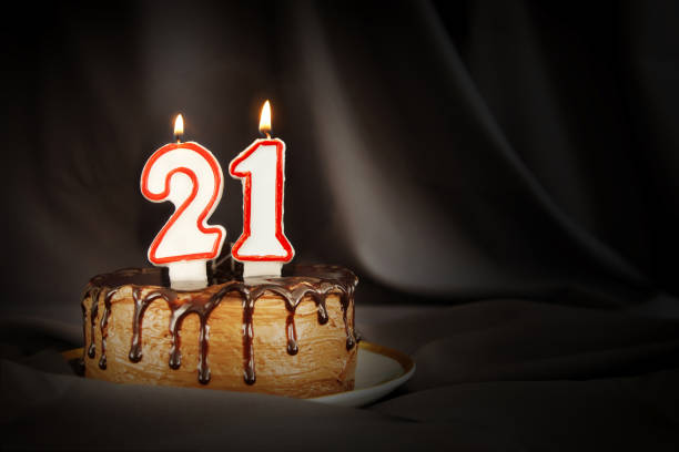 Twenty one years anniversary. Birthday chocolate cake with white burning candles in the form of number Twenty one. Dark background with black cloth