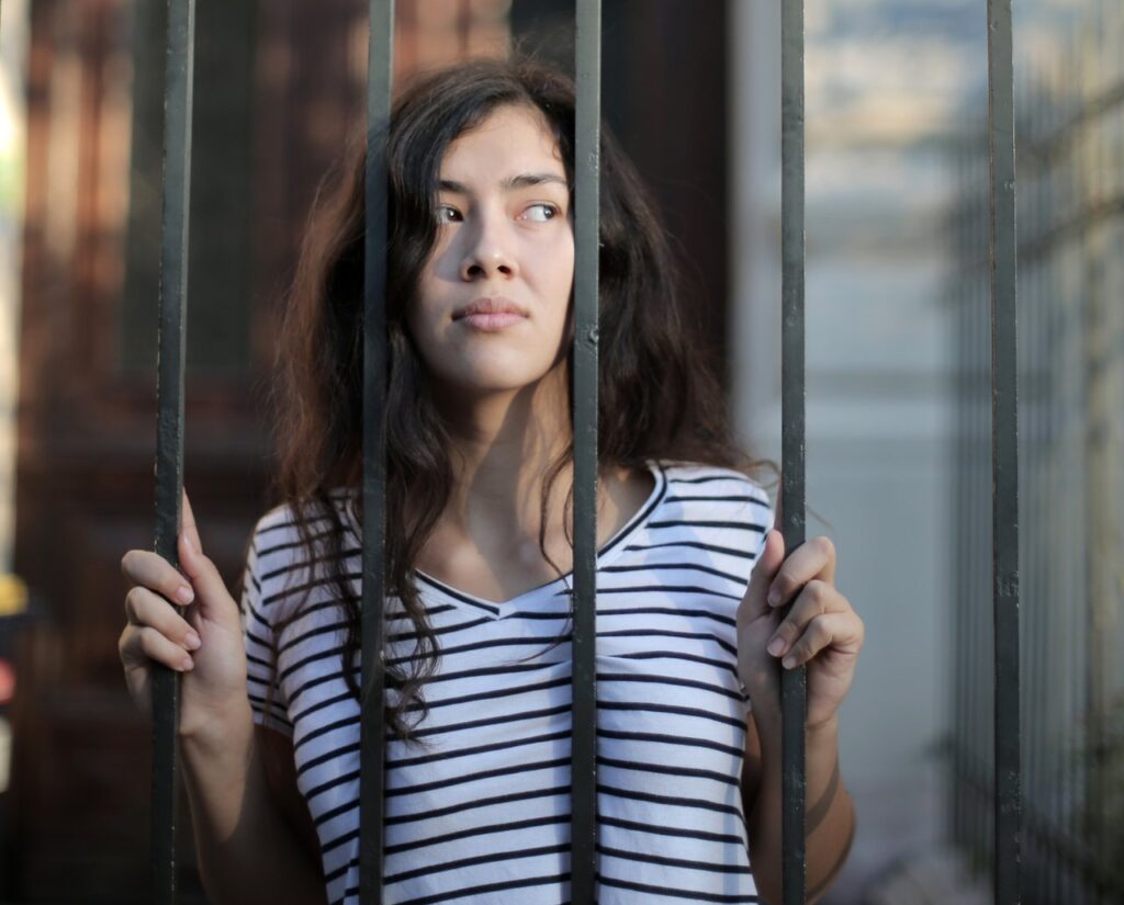 Curious Isolated Young Woman Looking Away Through Metal Bars 3808801 E1596447859361