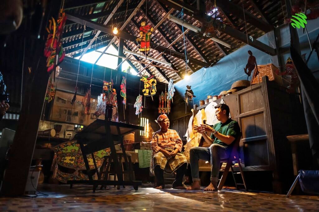 A Practitioner Of Wayang Kulit Sits Down In His House Talking To An Interviewer.