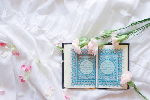 Islam Quran Open On A White Bed, With Flowers Laid On Top.