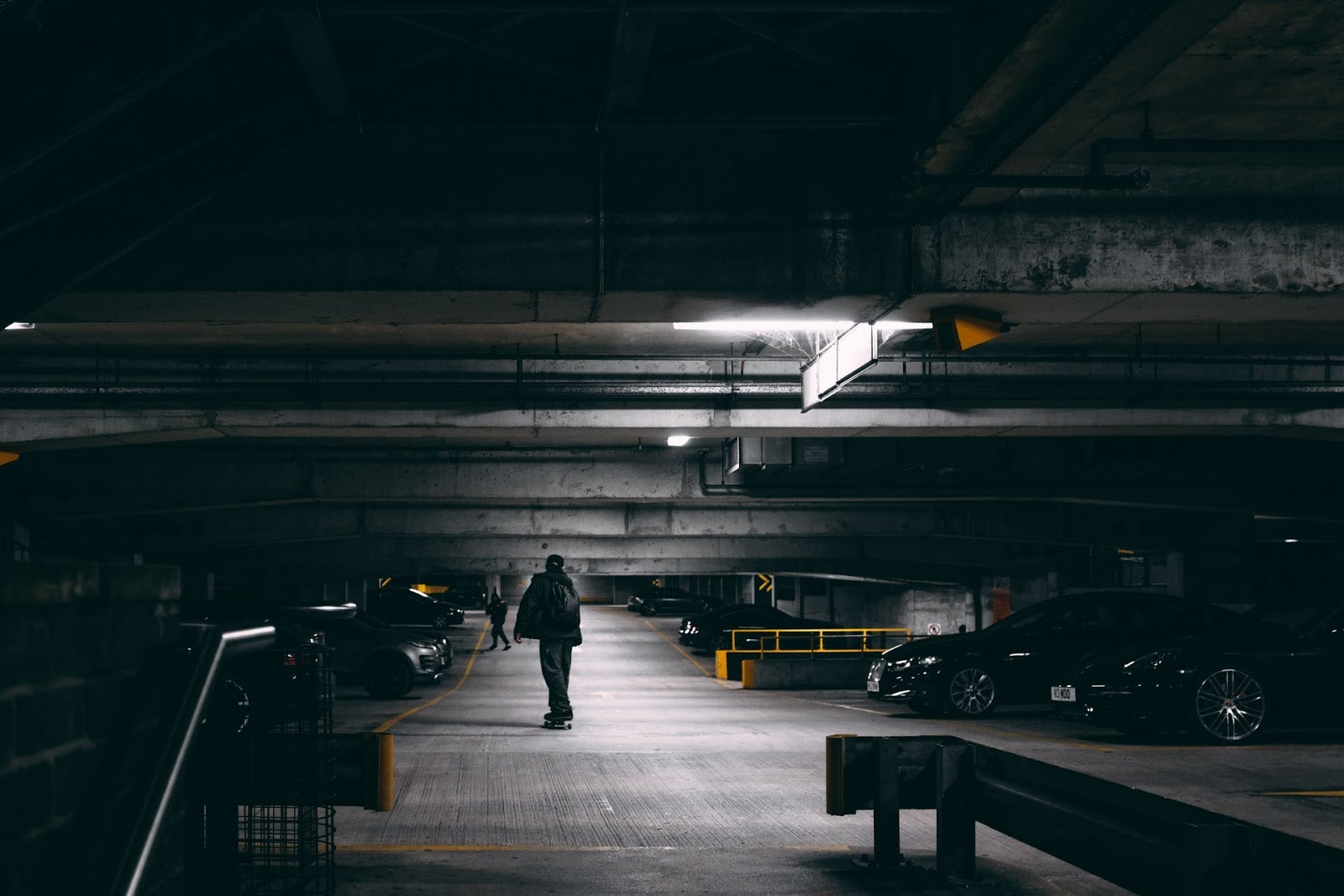 A darkened carpark where a lone man is watching someone getting into a car.