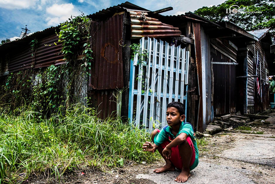 A boy squatting outside a delapidated rural house
