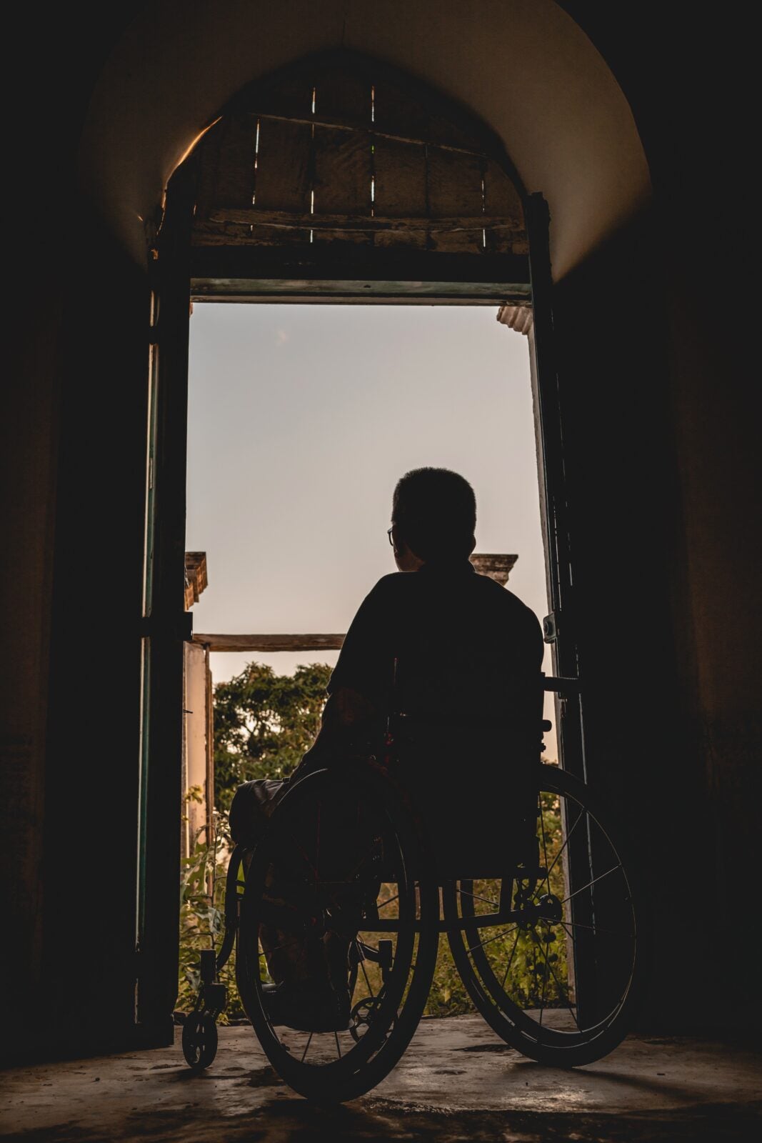 man in wheelchair gazing out huge open windows