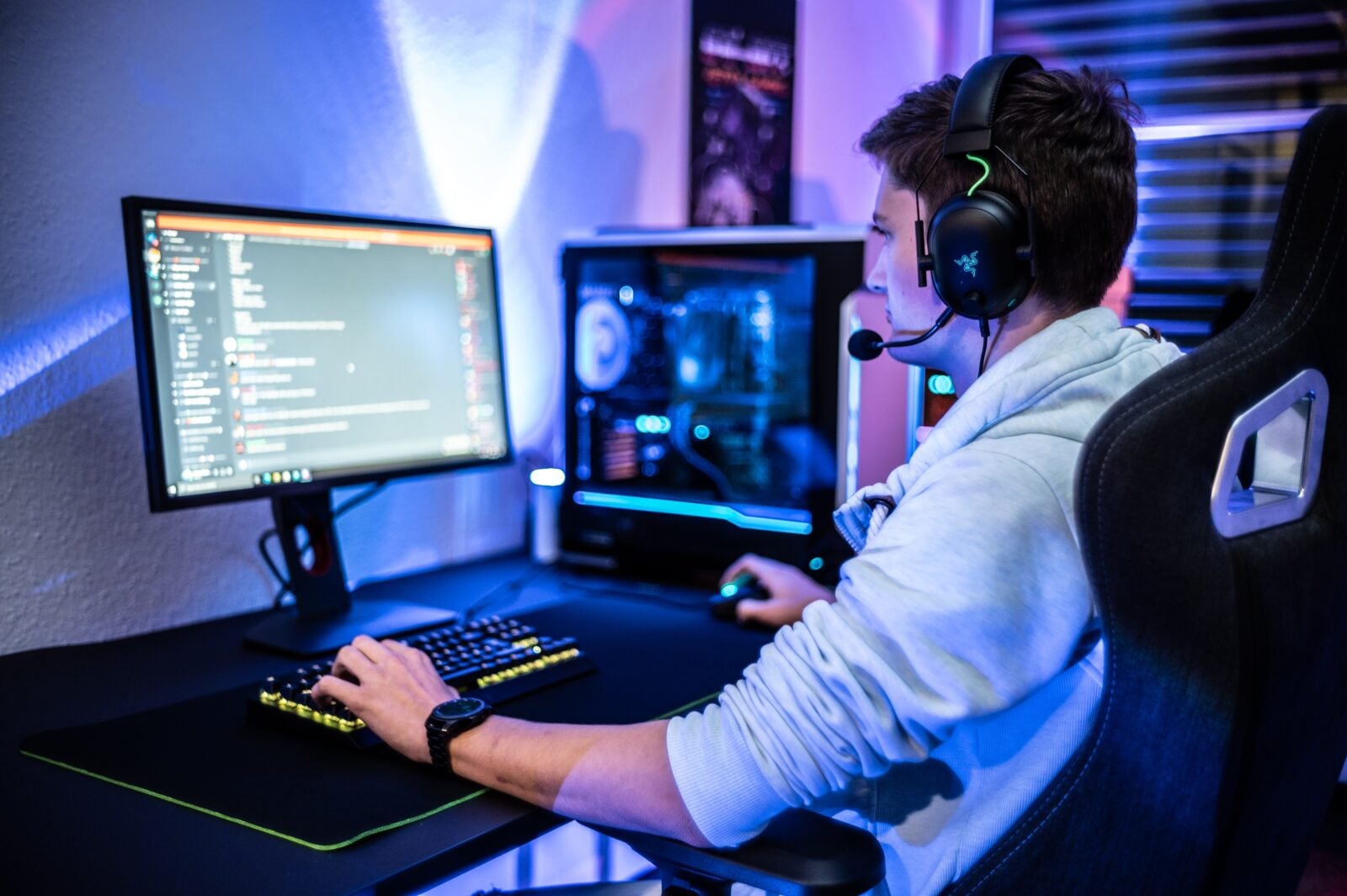 A man sitting in front of his computer with a fancy looking desktop, wearing a headphone and playing a game.