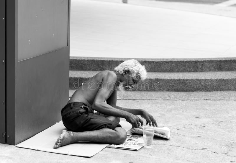 A homeless man sitting on the ground in public.