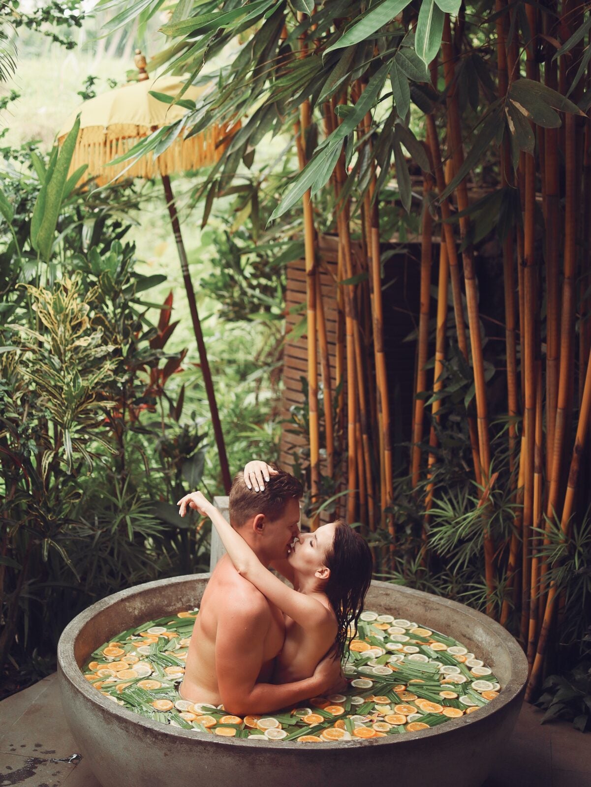 A couple in a round tub filled with water and flowers. They are kissing and hugging.