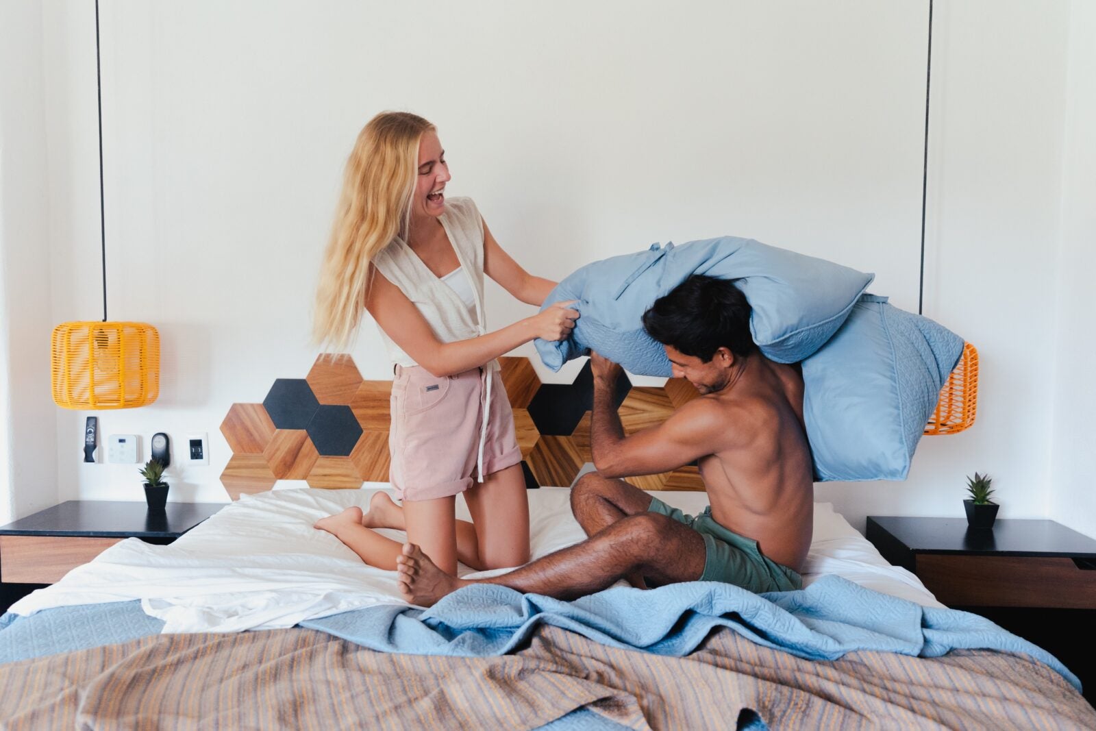 A couple in bed. The woman is hitting the man with a pillow while laughing.