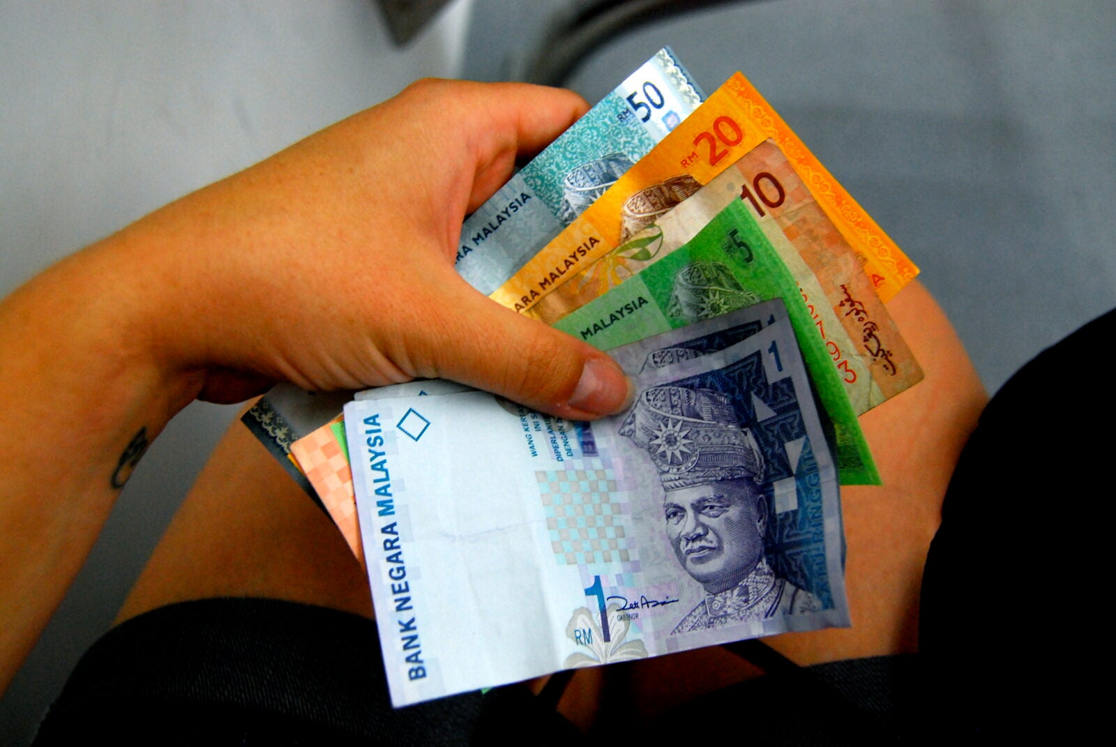 A hand holding RM77 worth of cash.