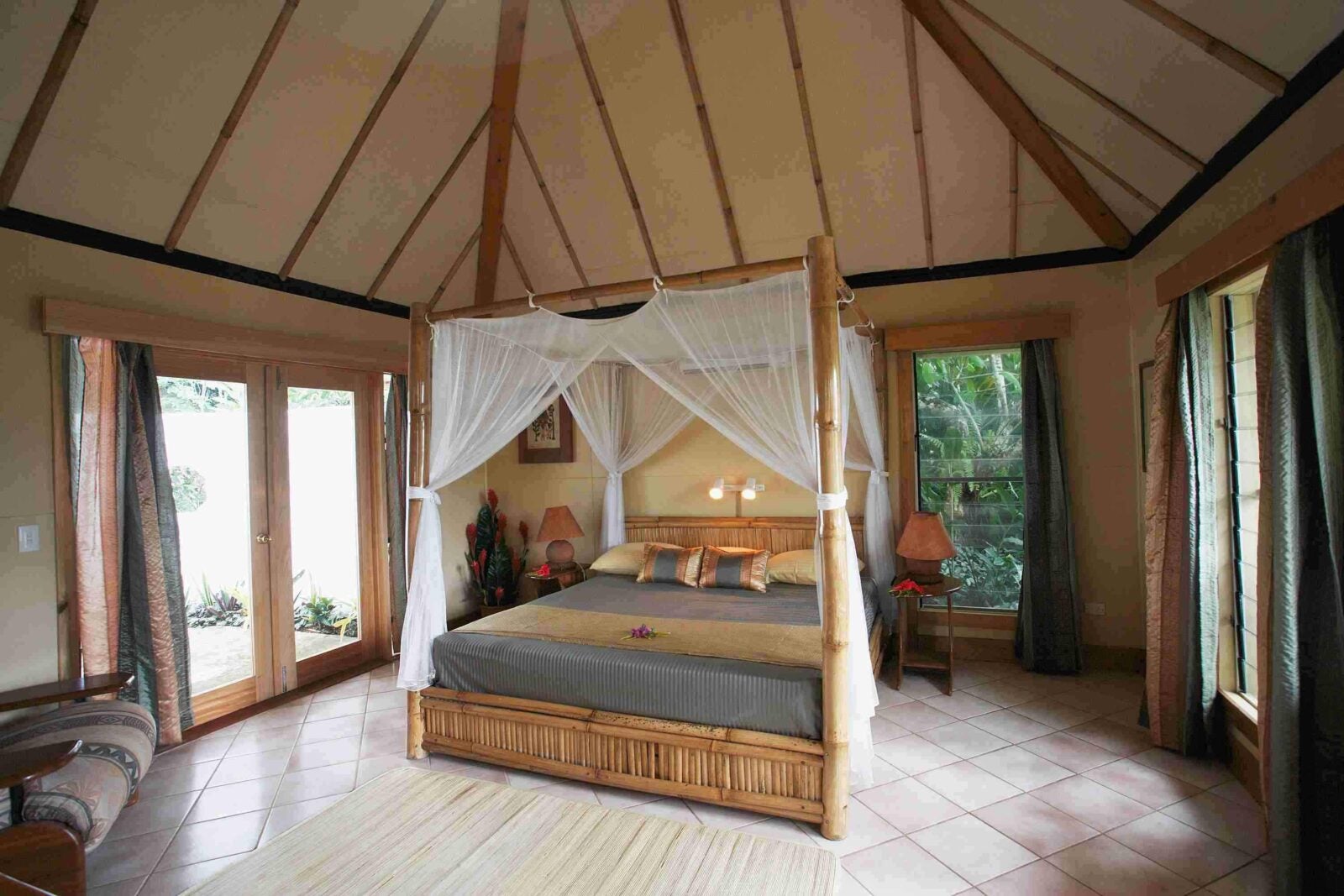 A king-sized bed with a canopy and white curtains in the middle of a big room with high ceiling.