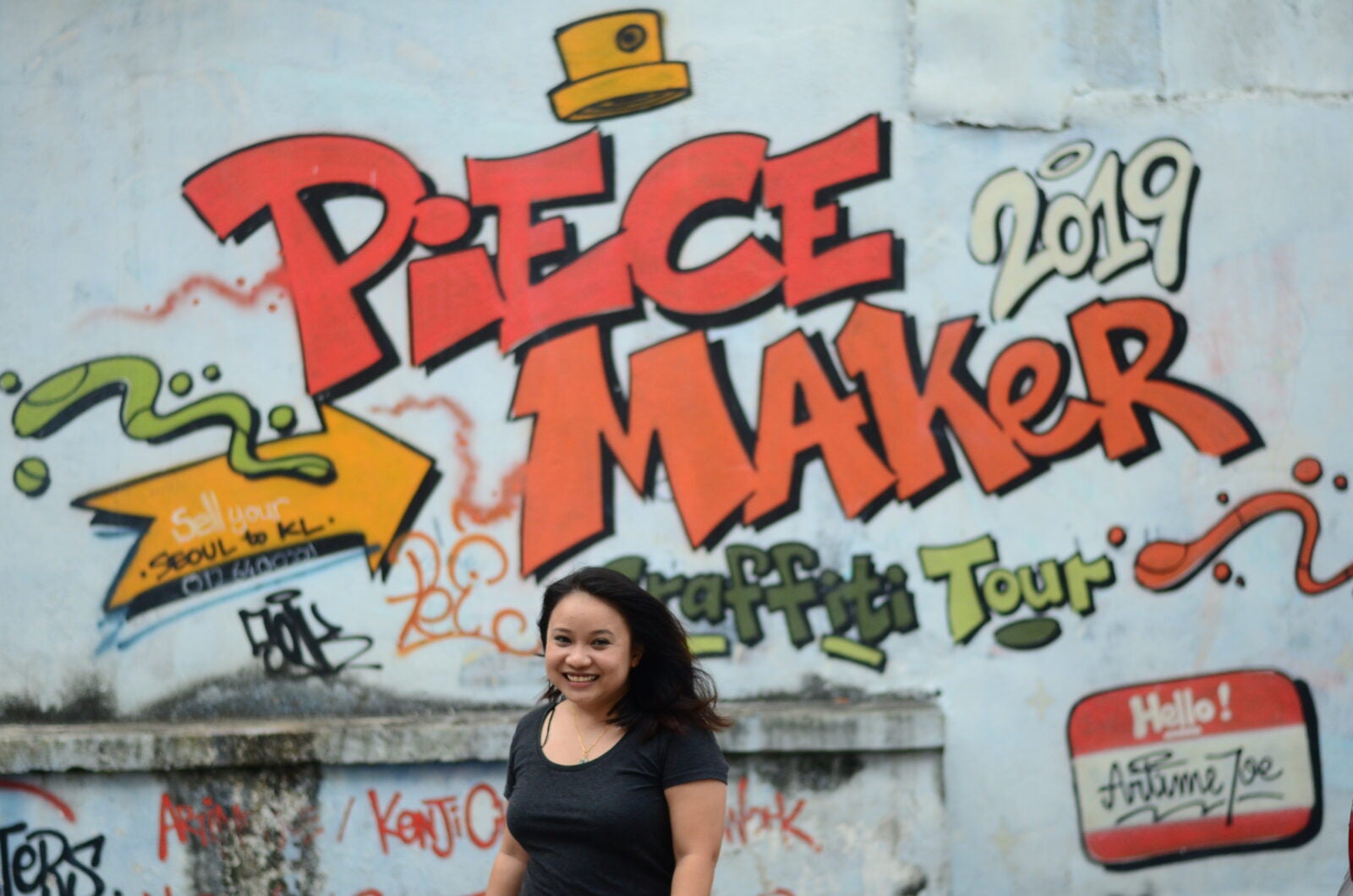 Maryam Lee, activist and feminist, standing in front of a graffitied wall that reads: "Peace Maker"