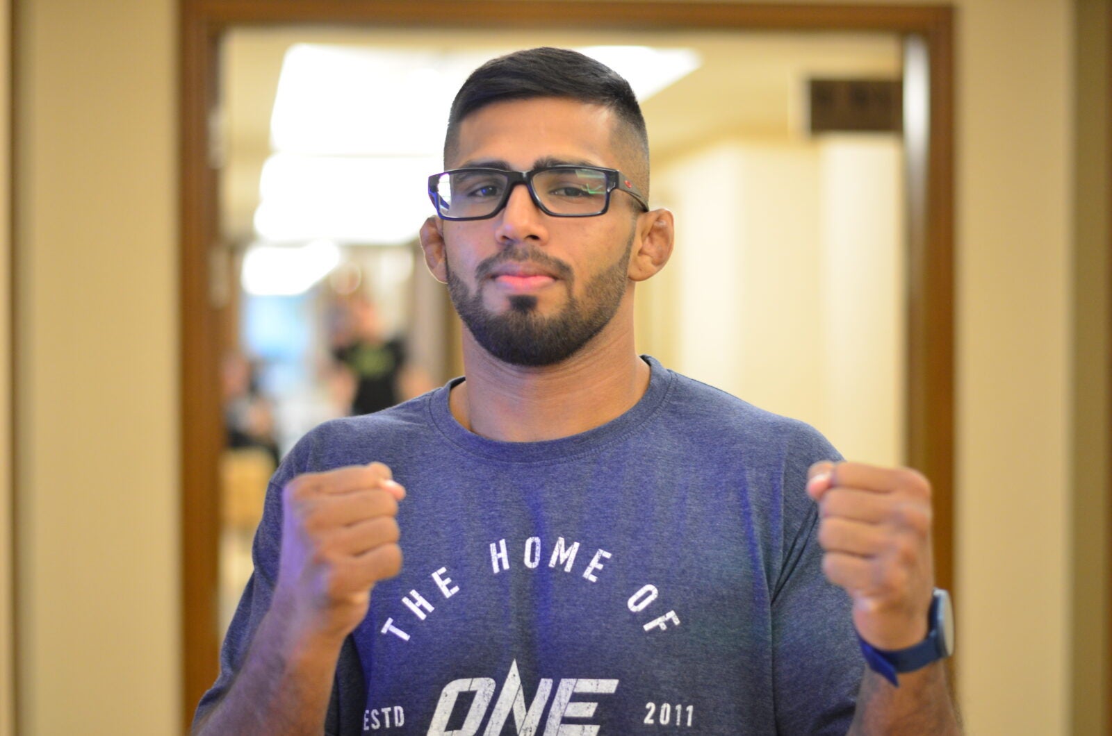 Agilan Thani doing a fighter pose and wearing glasses and a blue shirt
