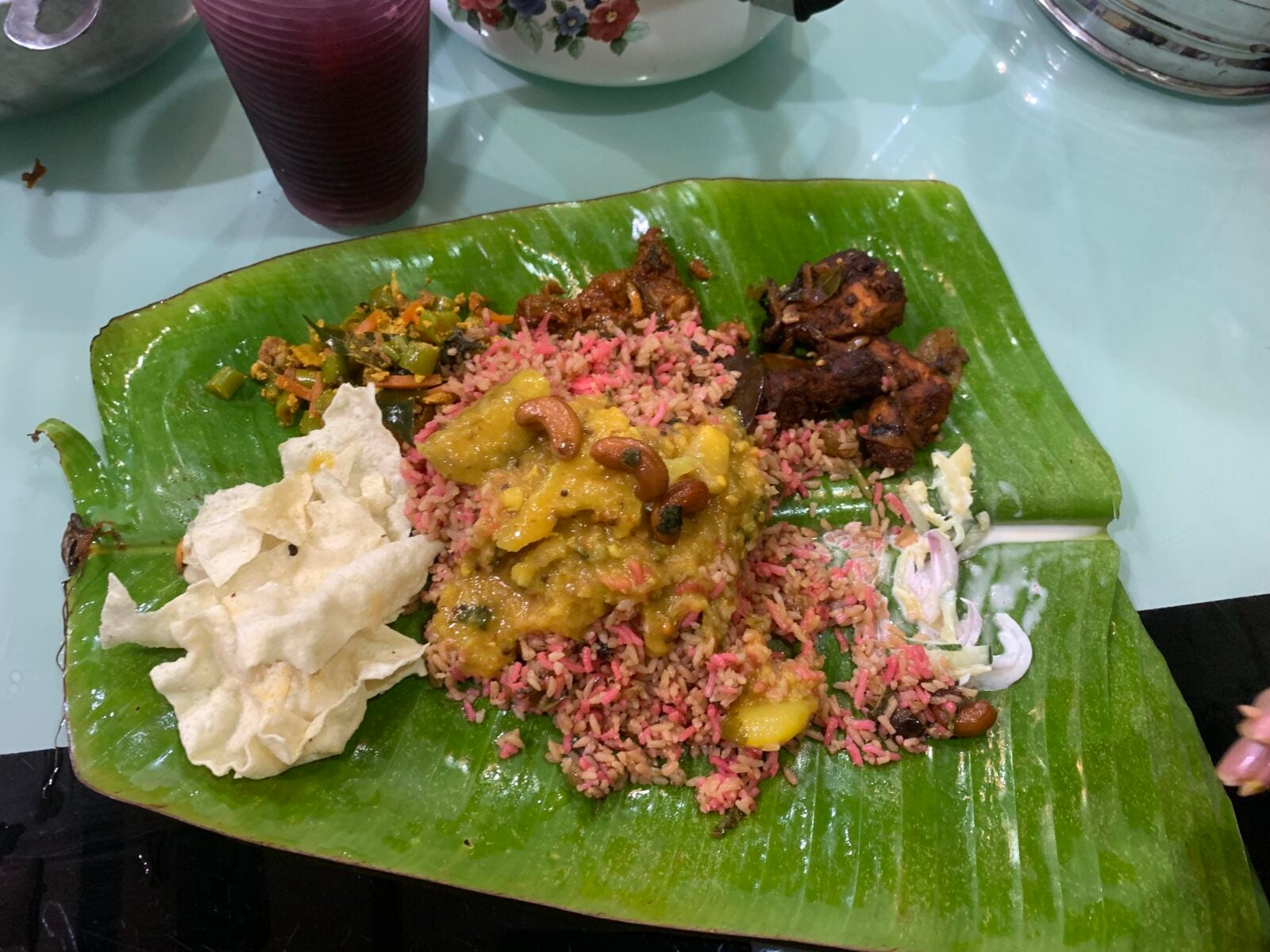 A banana leaf serving of Indian dish including nasi hujan, papadam, mutton curry, chicken 65, dhaal and yoghurt vegetable.