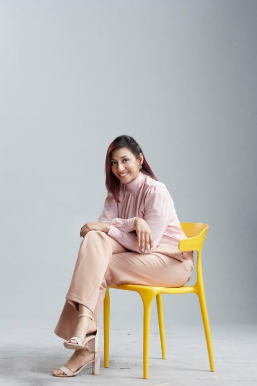 Navi Indran Pillai, a Malaysian Indian breast cancer survivor sitting on a yellow chair wearing pink clothes.