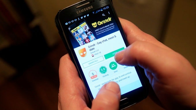 A Man Using His Phone To Download The Gay Dating App, Grindr.