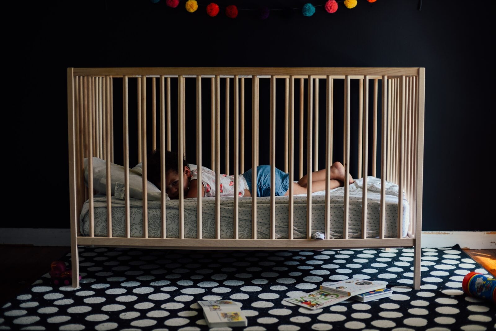 A toddler laying in his wooden crib.