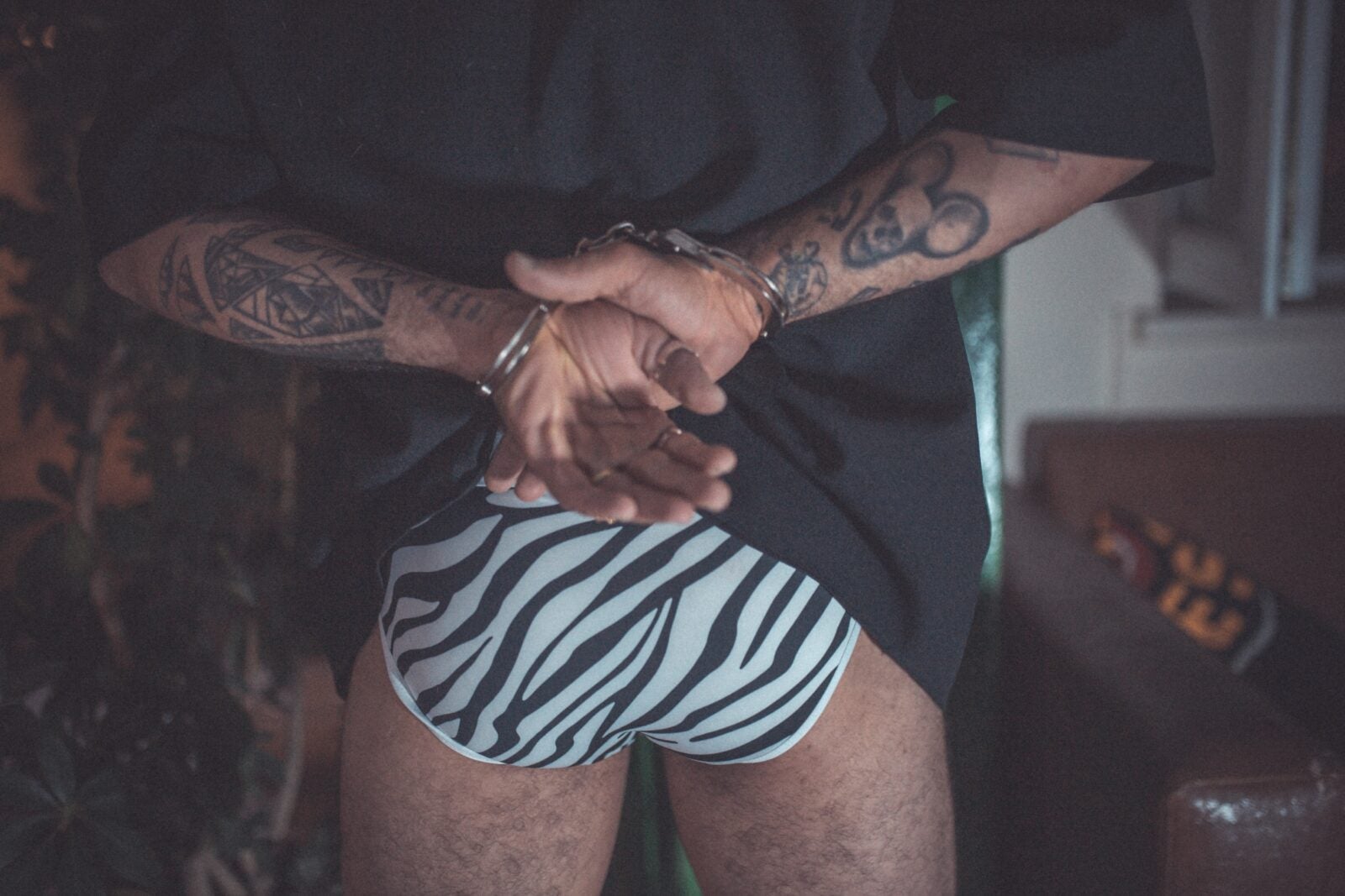 A Man Wearing Zebra Stripped Underwear With His Hands Handcuffed Behind Him.
