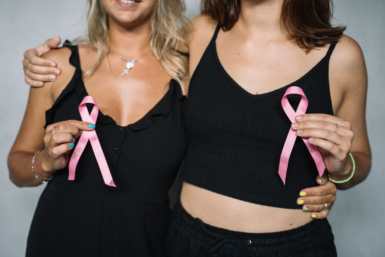 Two women wearing black tanktop and holding onto a pink ribbon for Breast Cancer Awareness.