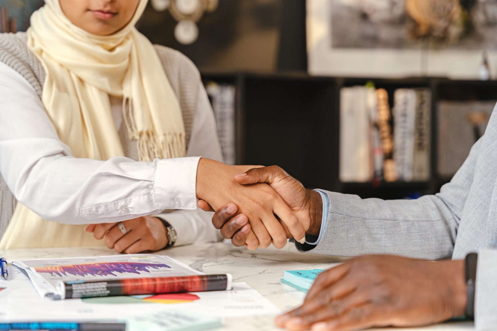 A cropped image of a woman wearing beige hijab shaking hands with a man.