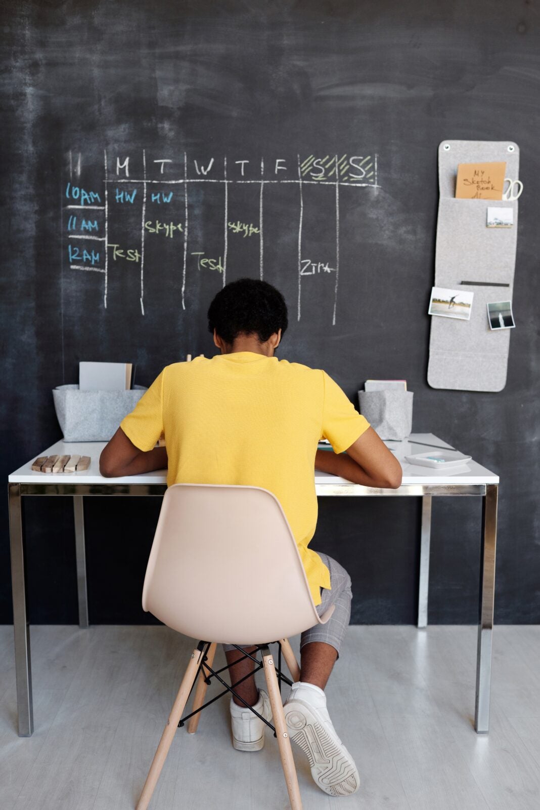 A Dark Skinned Boy Sitting In Front Of A Blackboard On A Study Desk.