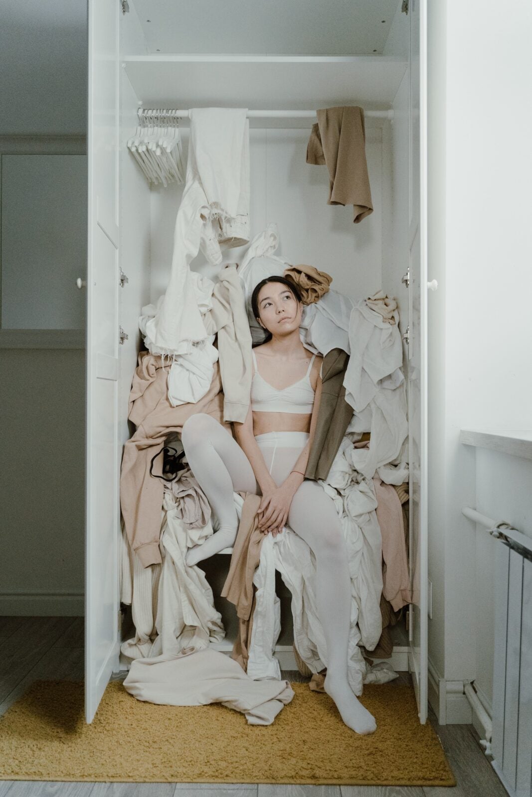 A woman sitting in her closet with clothes messy on her.