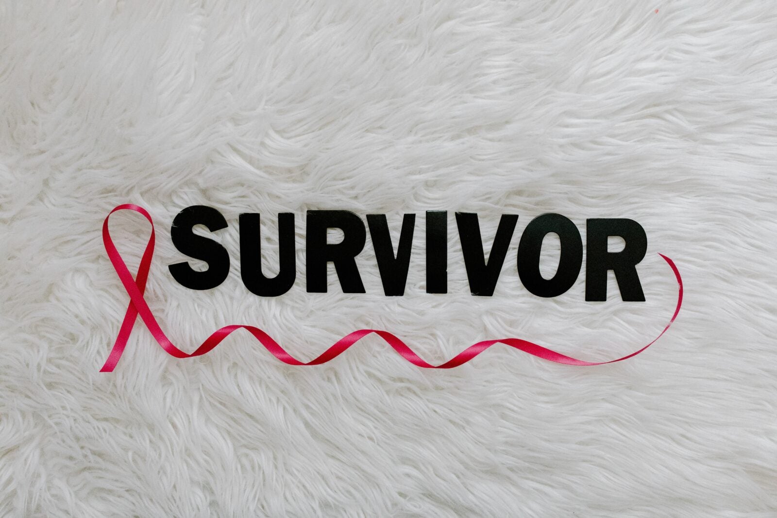 A pink ribbon and the word "Survivor" on a white fur carpet.