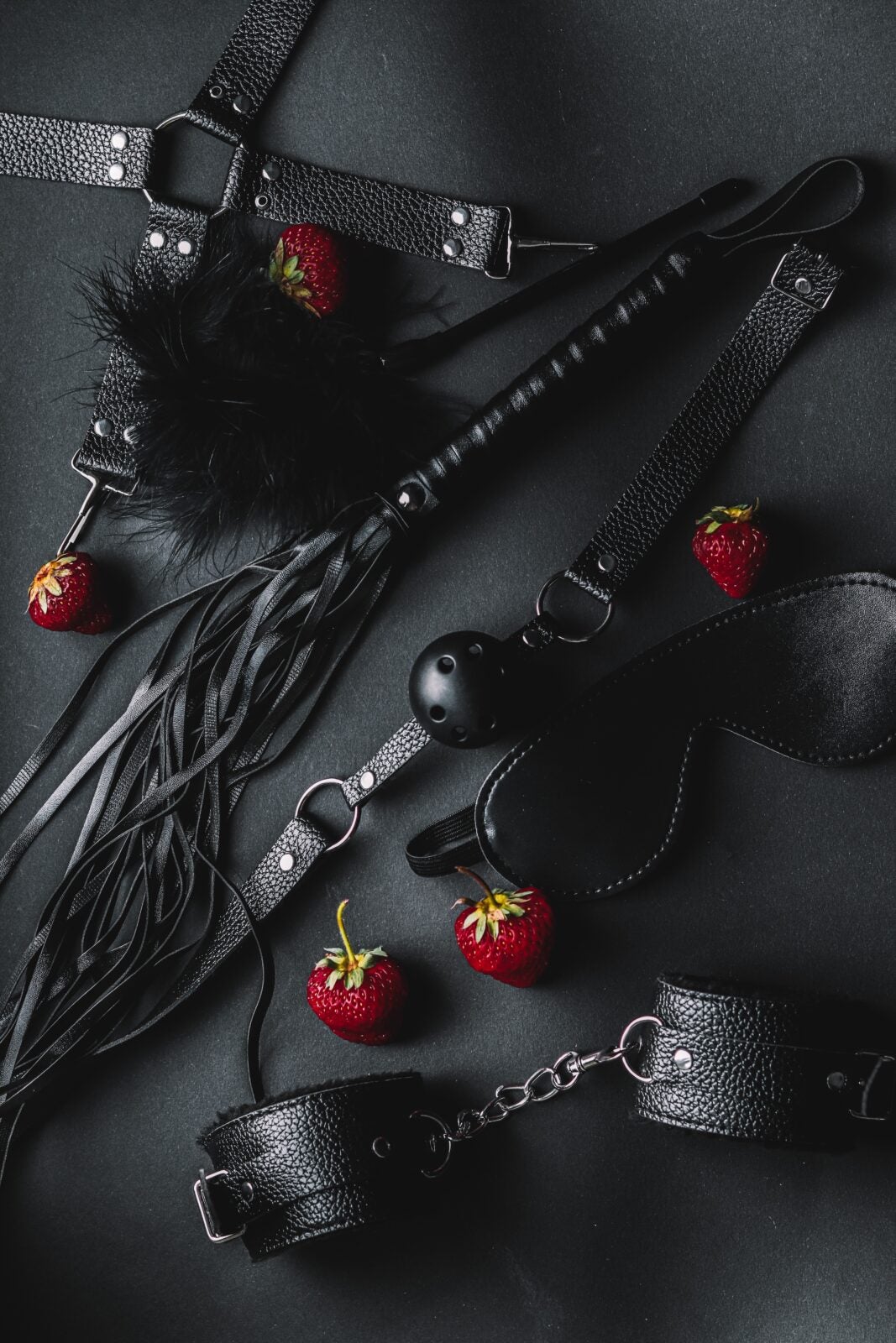 An Assortment Of Bdsm Equipments Including A Whip, Handcuffs, A Mouth Gag And A Blindfold.