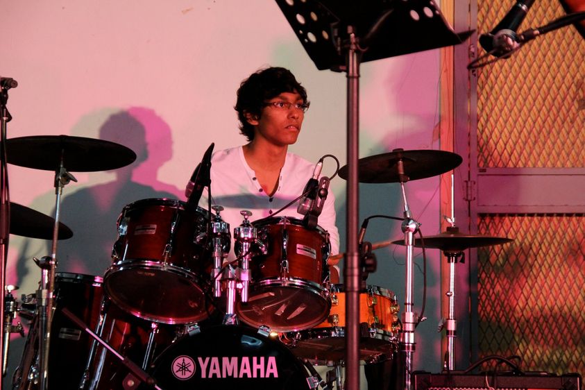A teenage Malaysian Indian boy playing the drums on a stage.
