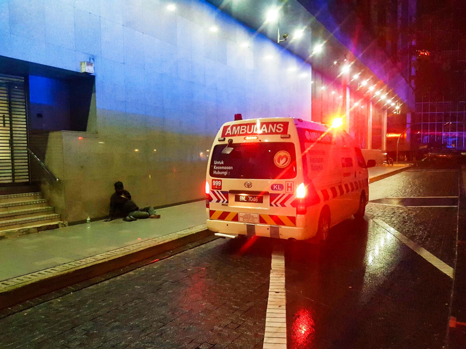 An ambulance parking at the side of the street, in front of a Homeless Malaysian Man.