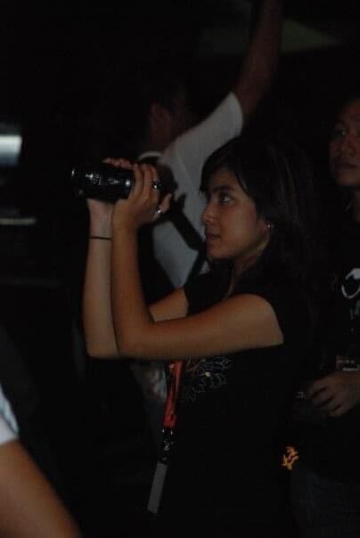 A petite Malay girl, Jeany who is holding a video camera while standing in the dark.