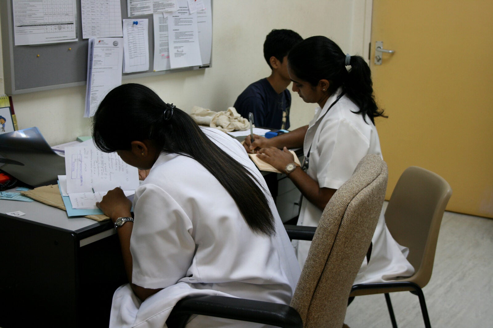 Two Malaysian Indian woman sitting at a desk and doing paperwork at a hospital.