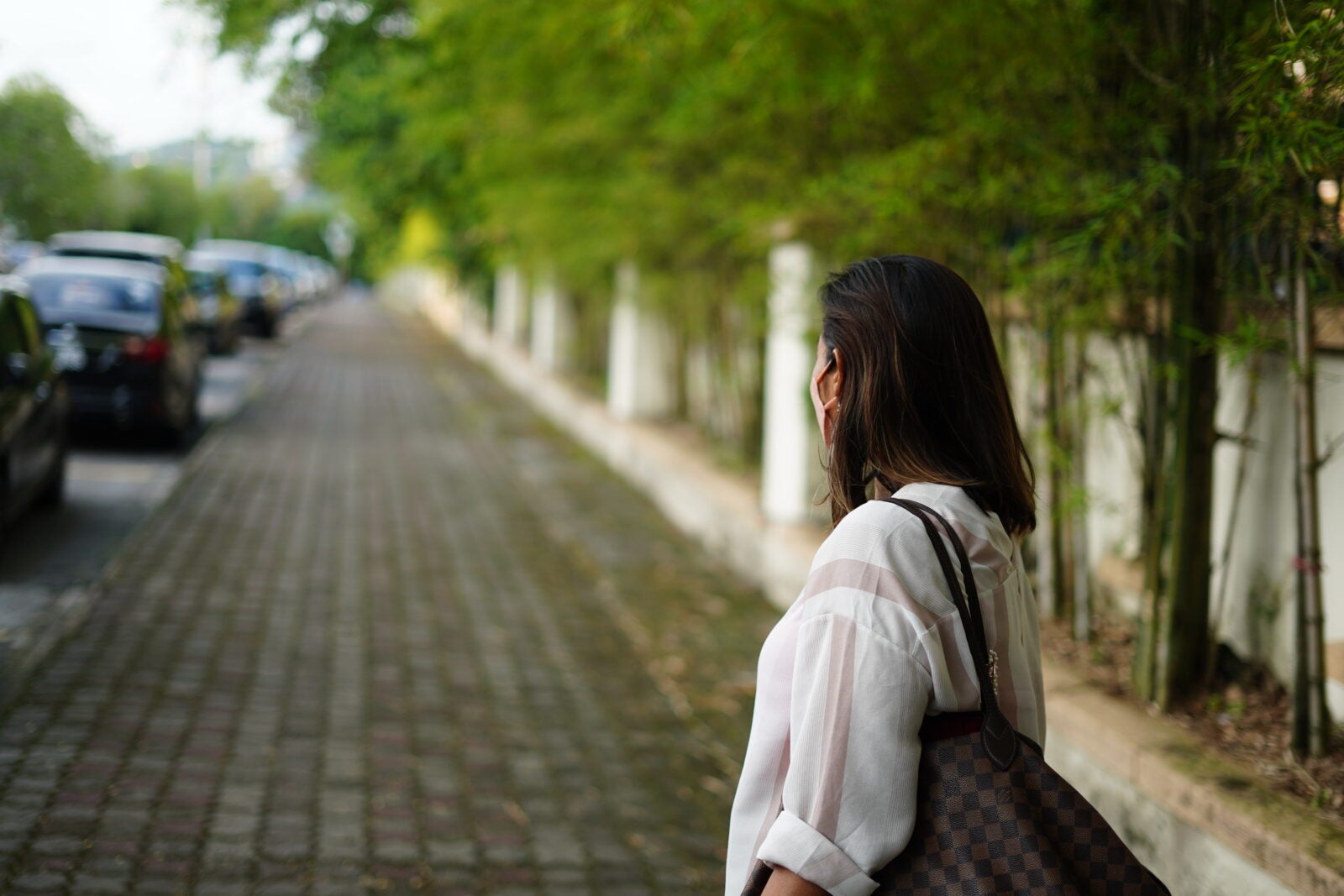Woman wearing white blouse standing on the sidewalk and looking behind her.