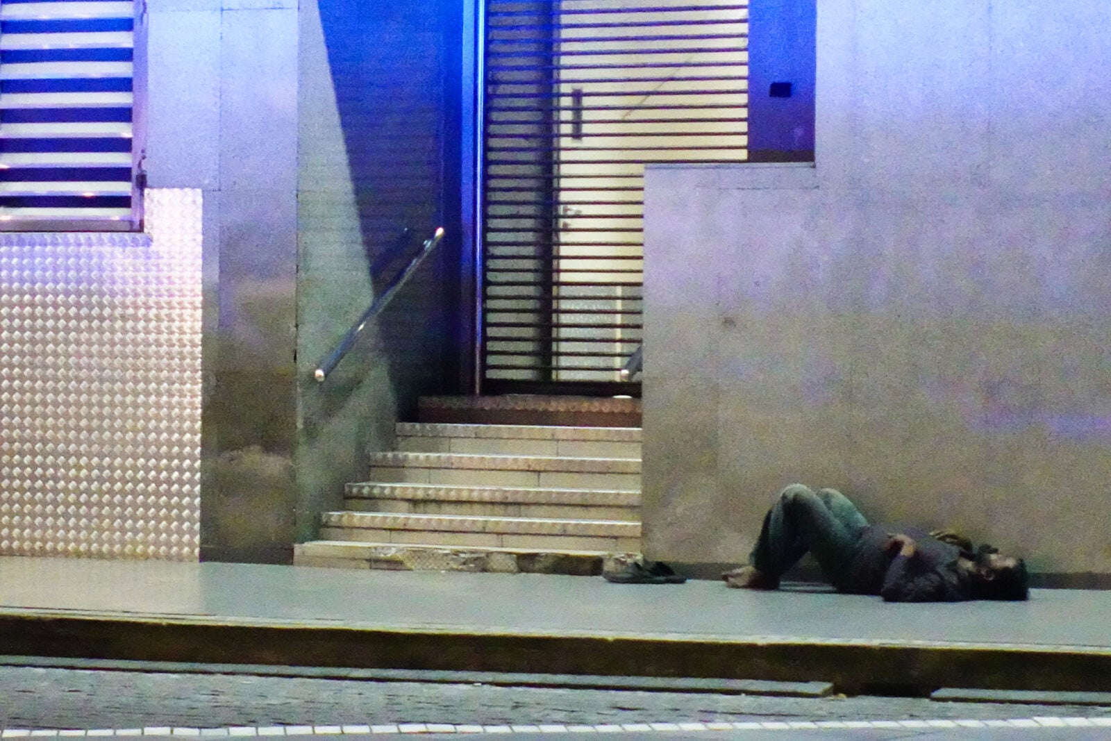 A homeless Malaysian man laying down on the floor in front of a building in Kuala Lumpur.