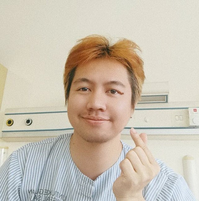 A Malay man with bleached hair posing while wearing a hospital gown.