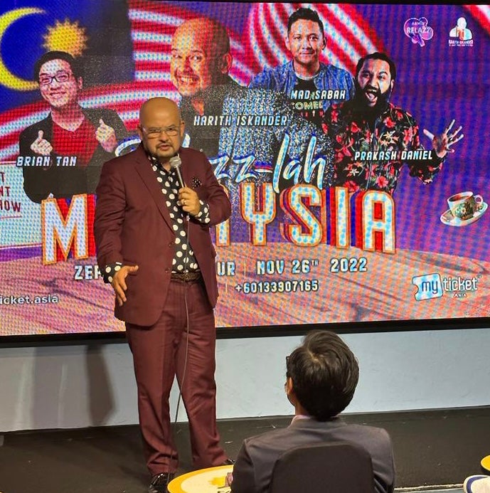 Harith Iskandar, A Malaysian Comedian Standing On Stage With A Microphone In Hand.