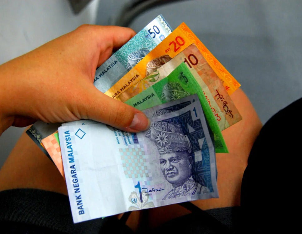 A hand holding money worth RM77.
