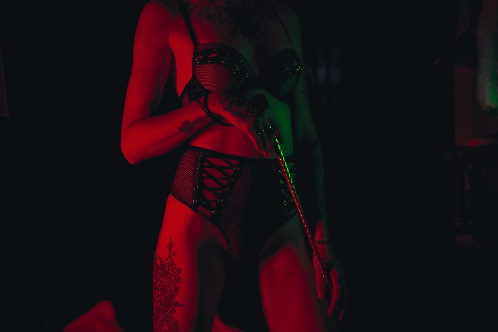 A woman dressed in lingerie and holding a whip in the dark illuminated with a dull red light.