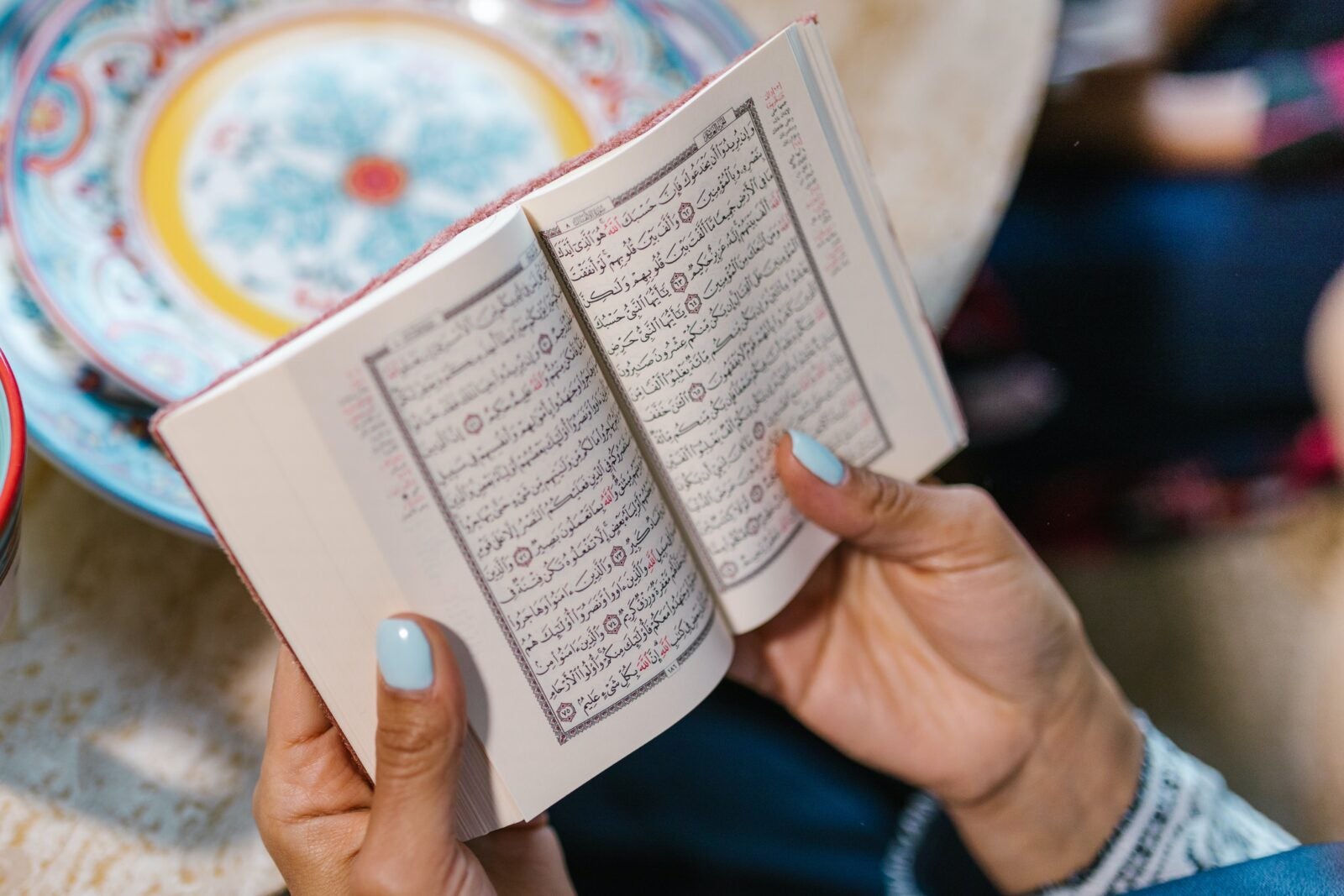 Close up of a woman's hand with blue painted nails holding a religious book.