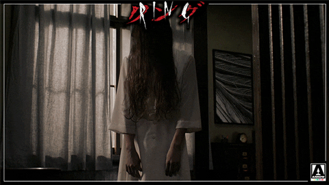 A creepy woman with long hair covering her face standing still and looking down.