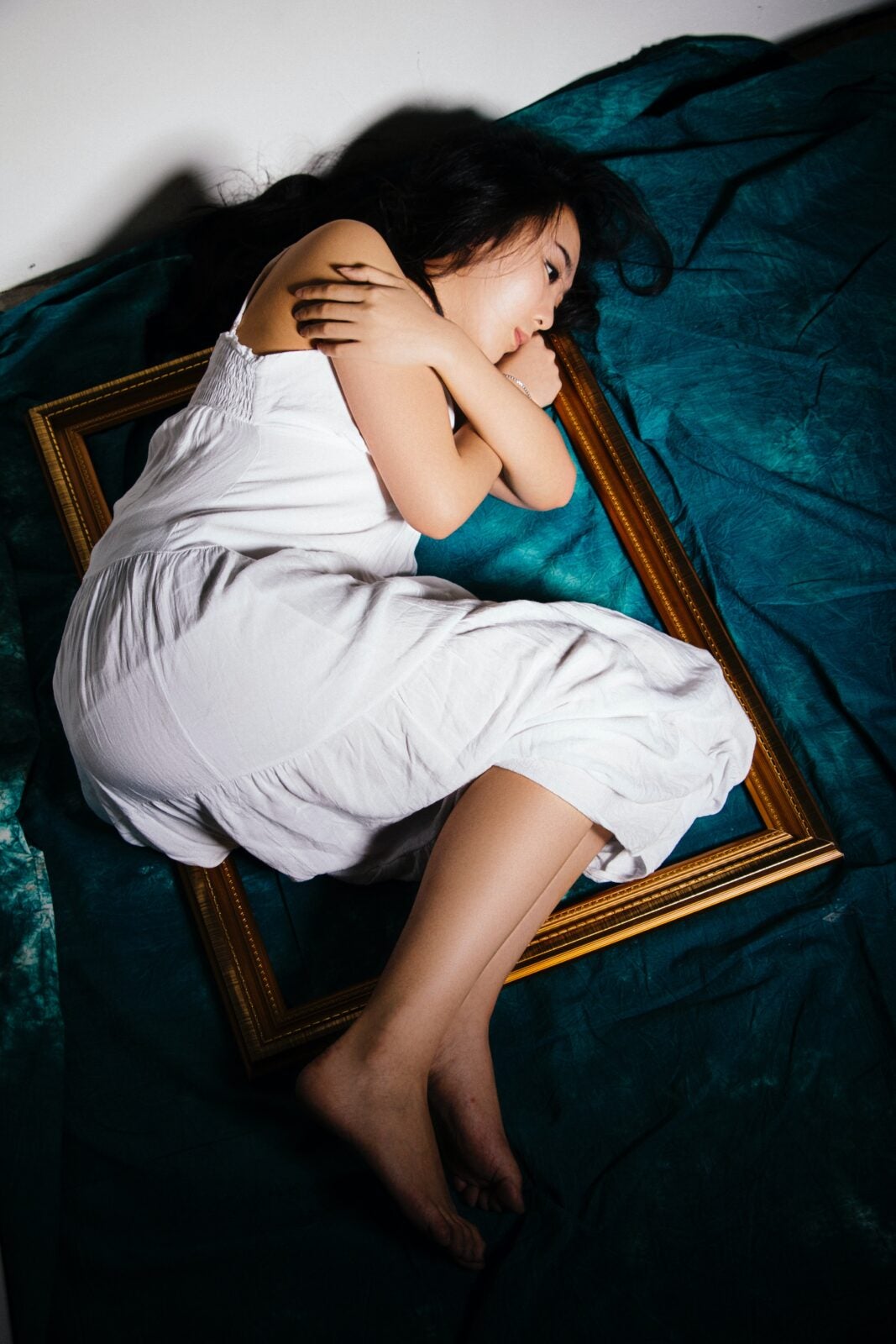 An Asian woman laying on top of a picture frame on a bed.