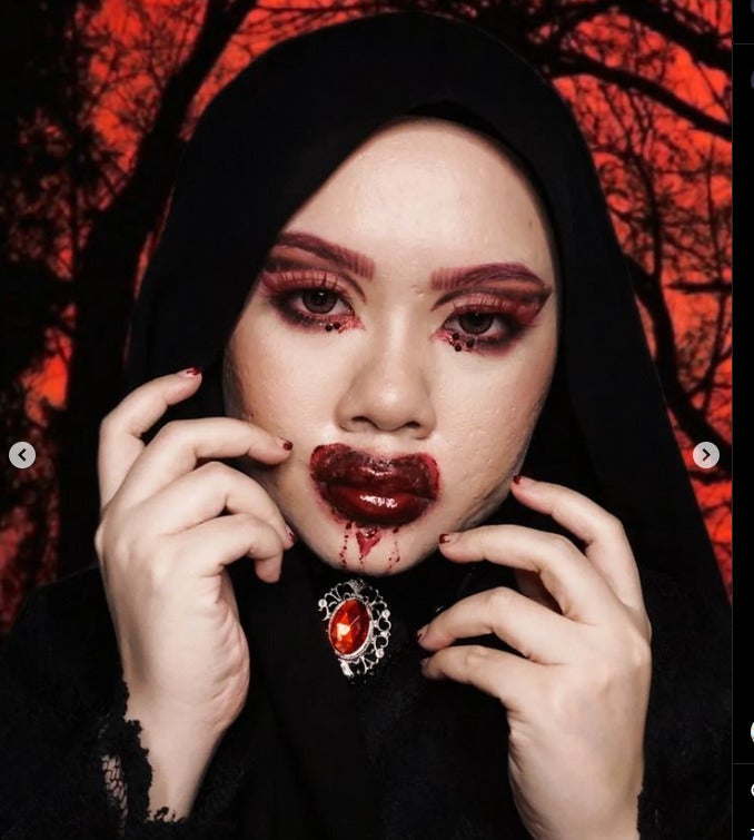 A Malay woman wearing the hijab and heavy makeup with blood stained lips and a red jewel for her brooch.