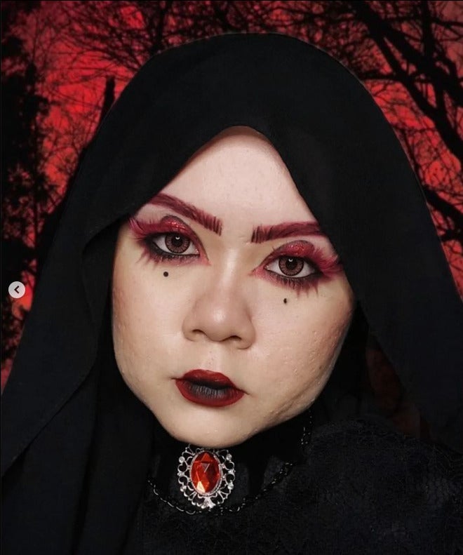 A Malay woman wearing the hijab and heavy makeup with a small beauty mark under each eyes, black and red lipsticks. and a red jewel for her brooch.