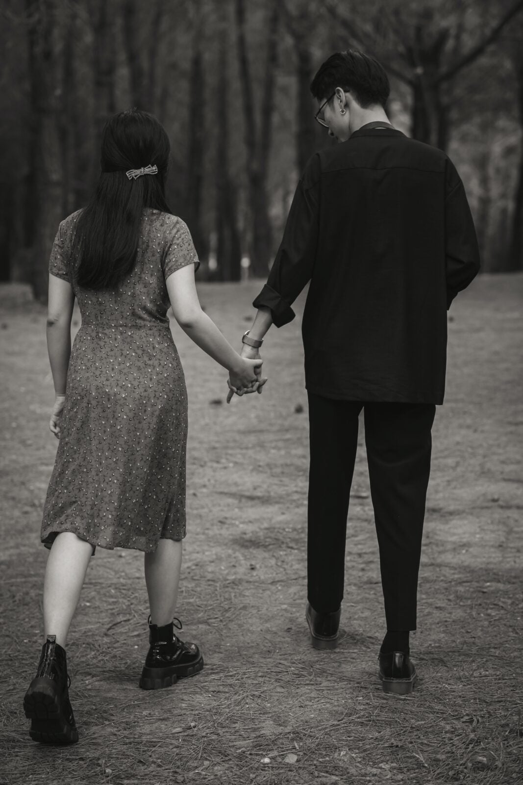 Black and white image of a woman in a dress and a man holding hands while walking in a park.