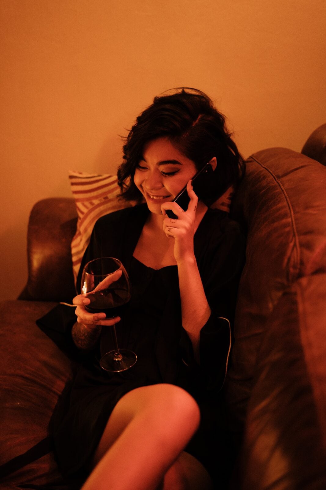 Young woman with short hair holding a wine glass and talking on the phone.