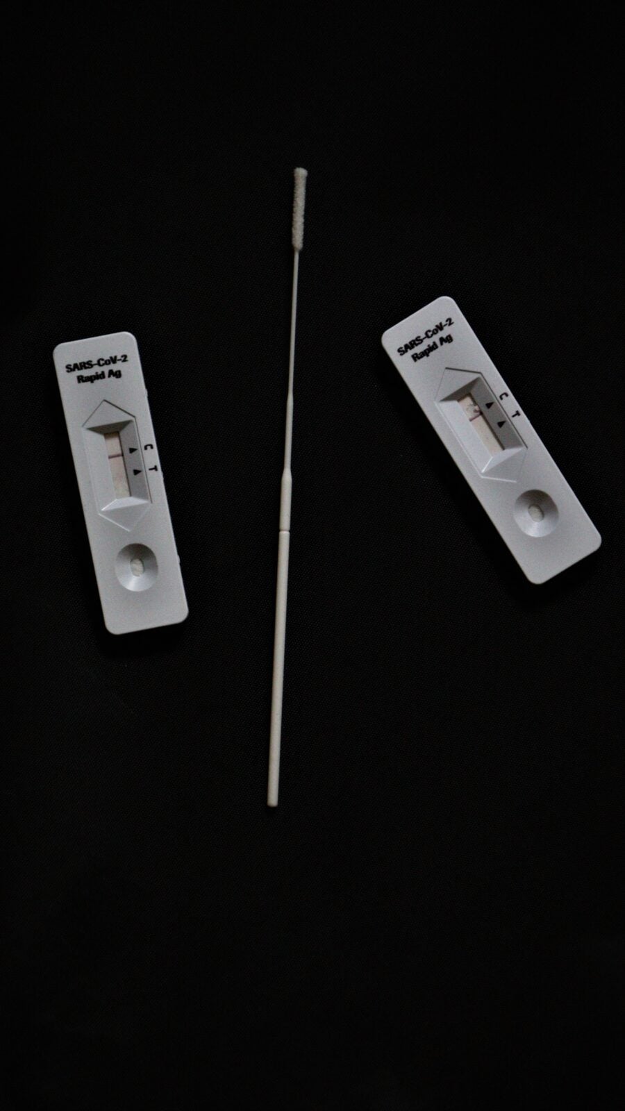 Two covid tests which shows the negative result separated by a nose stick between them.