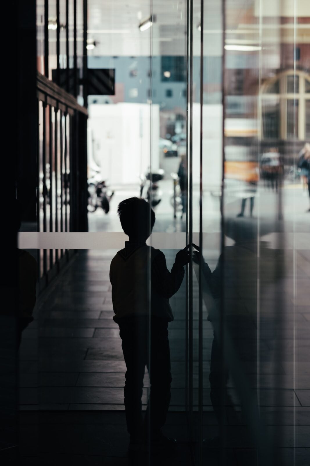 Silhoutte of a young boy in front of a glass door in a dark hallway.