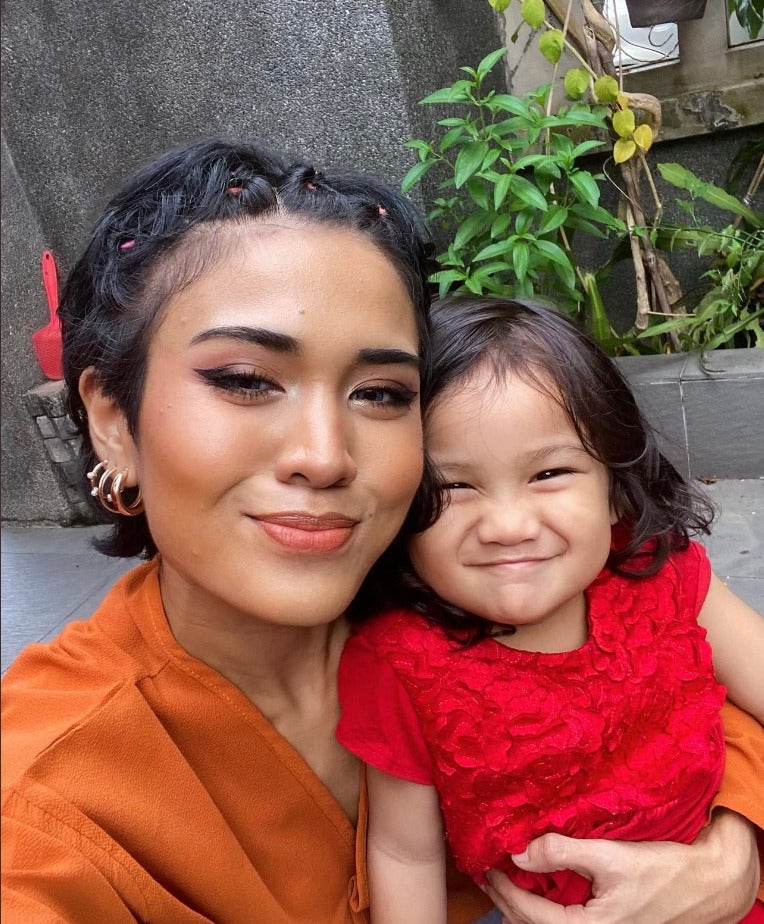 An Asian woman with short hair smiling with her daughter who is held tightly next to her.