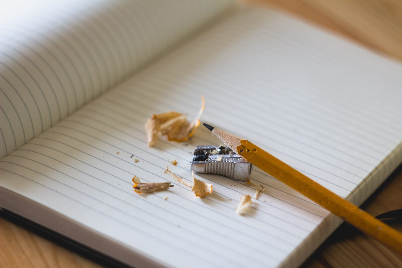 A pencil that is sharpened using a handheld pencil sharpener on a notebook. The residuals of the sharpened pencil lay messy on the notebook.